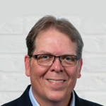 Brett Keown A man in glasses is smiling in front of a brick wall.