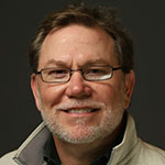 A man wearing glasses and a gray jacket.